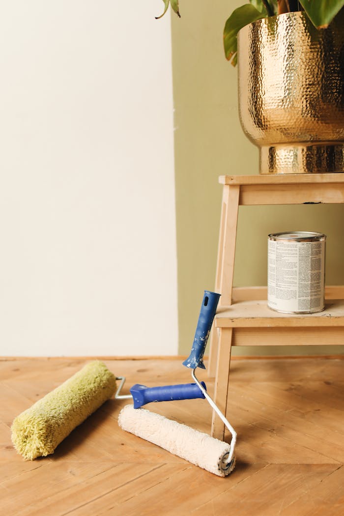 A stylish setup showcasing paint rollers, a step stool, and a golden planter on a wooden floor.